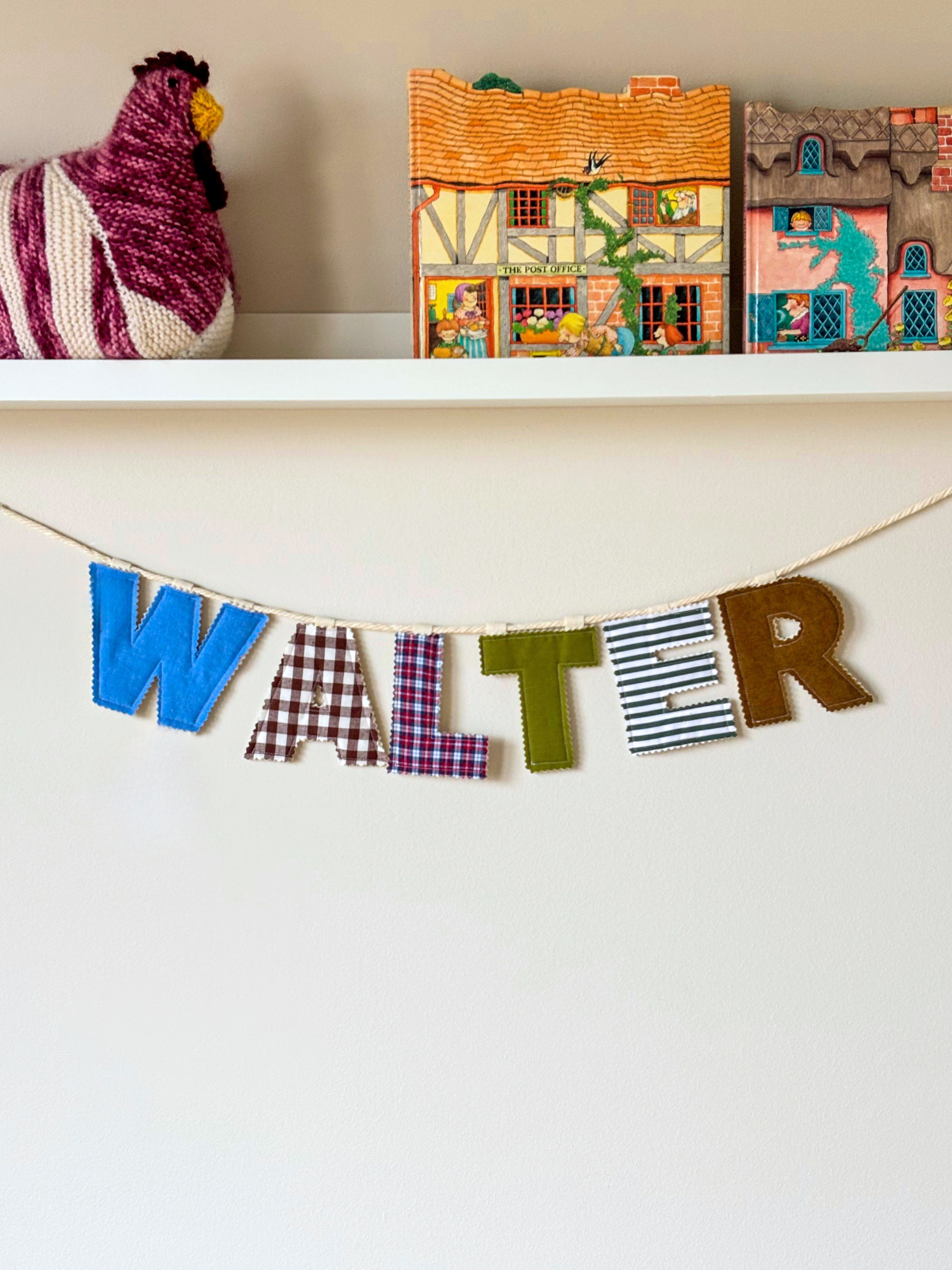 Personalised name banner spelling 'WALTER' in autumnal fabrics on a white wall. Made by Bugalugs in Melbourne. 