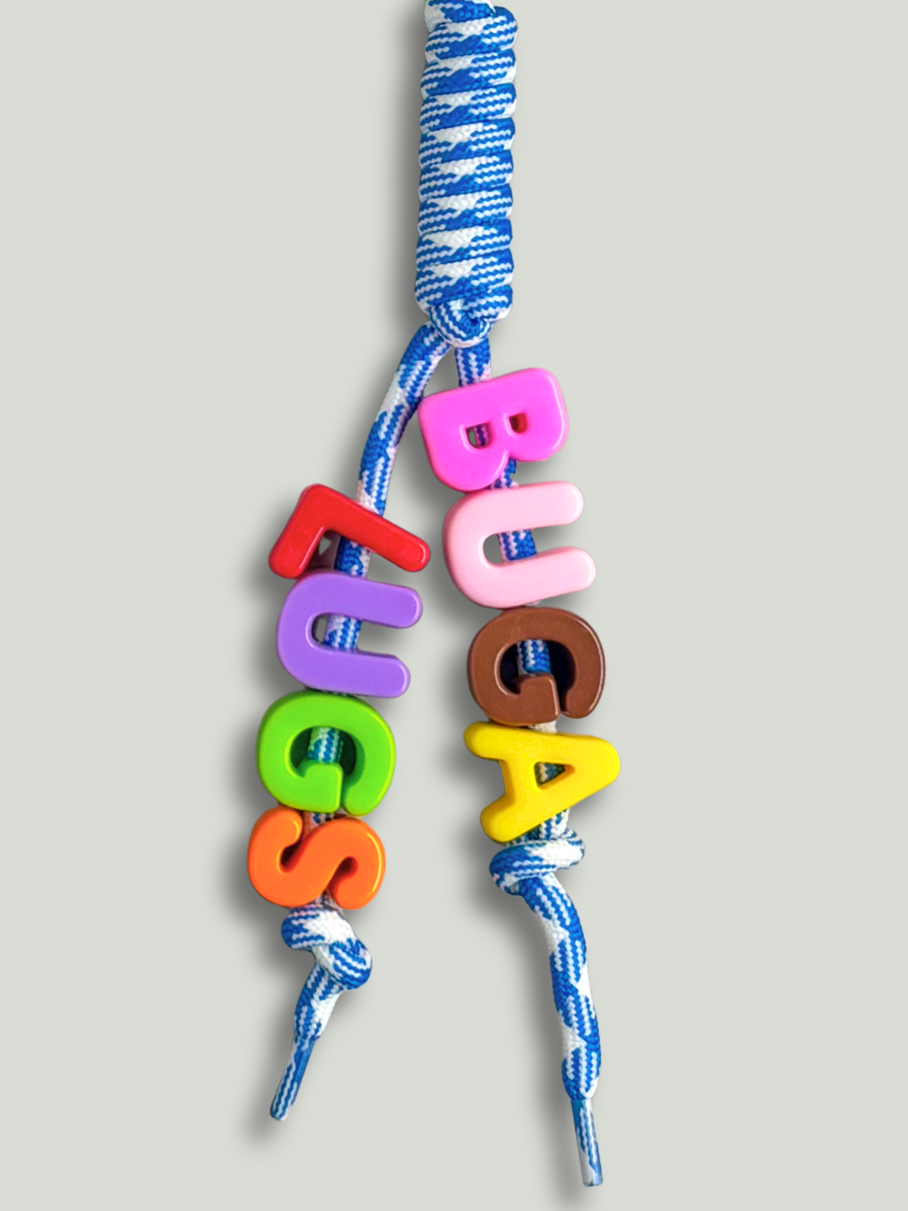 Custom statement bag charm with letter beads spelling BUGALUGS in pink, brown, yellow, red, purple, green and orange, threaded across two strands of a blue and white houndstooth knotted cord, on a gray background. Made by Bugalugs in Melbourne.