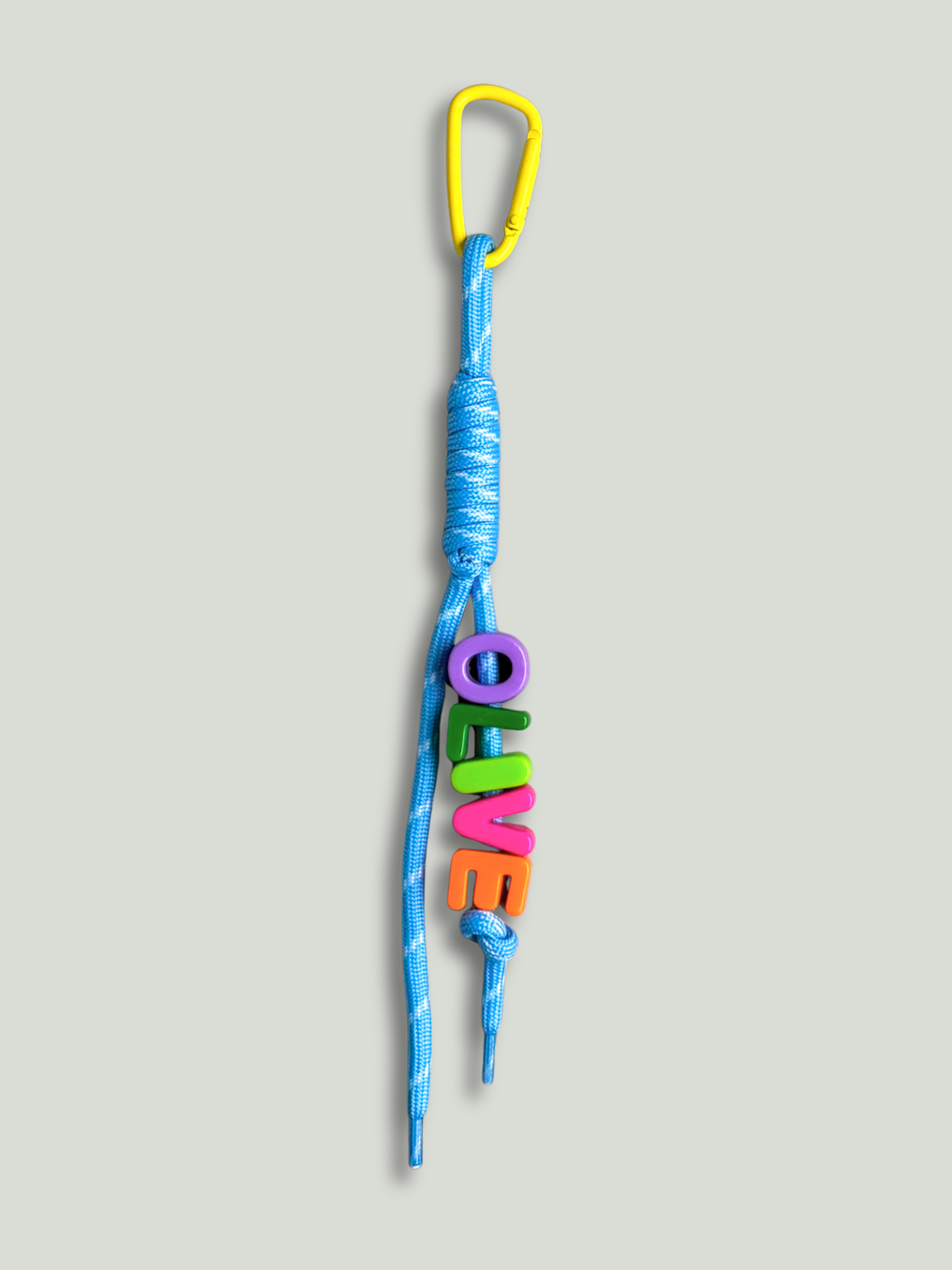 Personalised bag charm with letter beads spelling OLIVE in purple, green, lime, pink and orange, threaded on a blue and white fleck knotted cord, with a yellow carabiner clip on a yellow background. Made by Bugalugs in Melbourne.