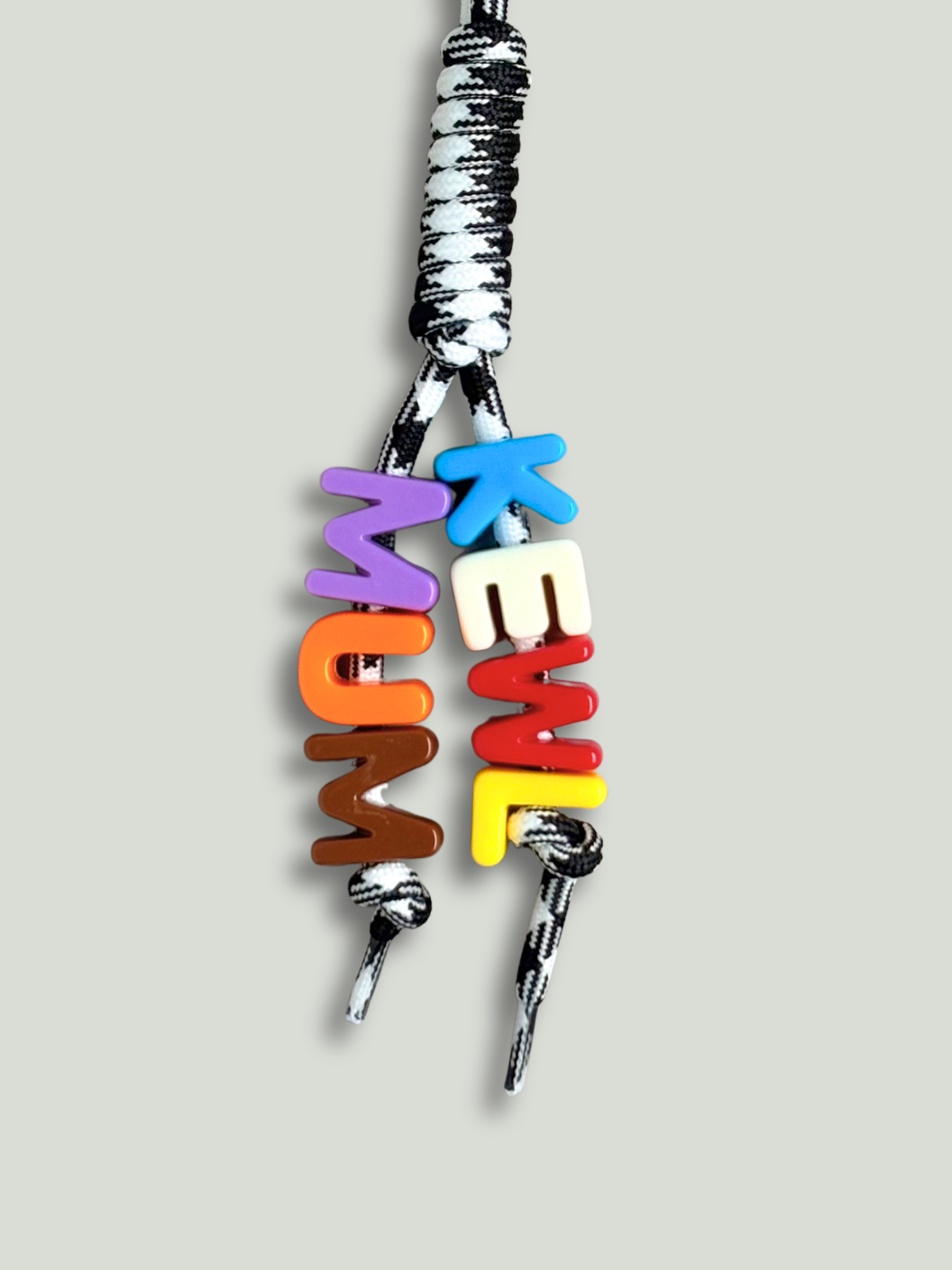 Custom statement bag charm with letter beads spelling KEWL MUM in blue, white, red, yellow, purple, orange, and brown, threaded across two strands of a black and white houndstooth knotted cord with a green carabiner clip, on a gray background. Made by Bugalugs in Melbourne. 