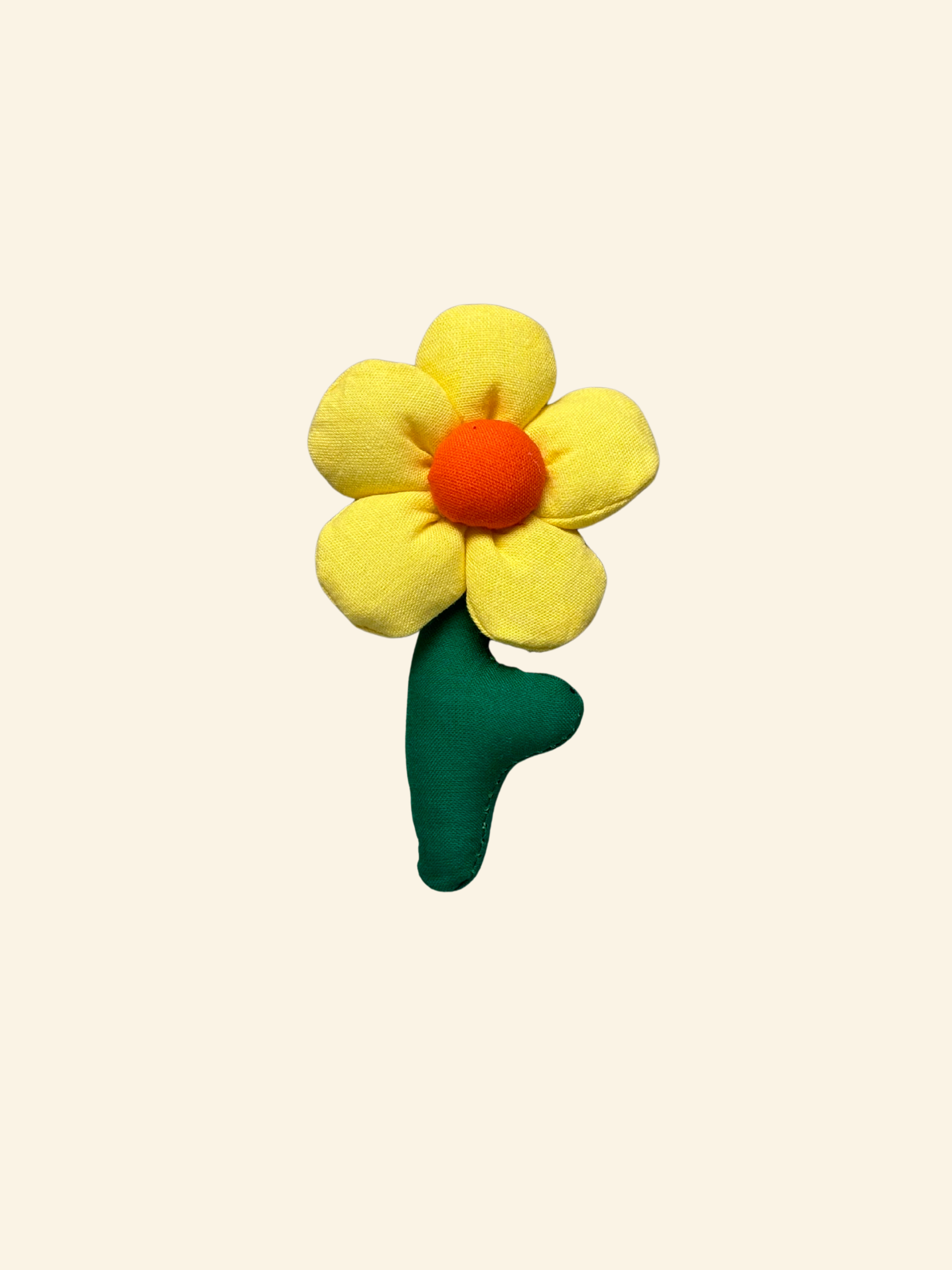 Puffy fabric daisy flower with yellow petals, orange centre, and green stem on a cream background